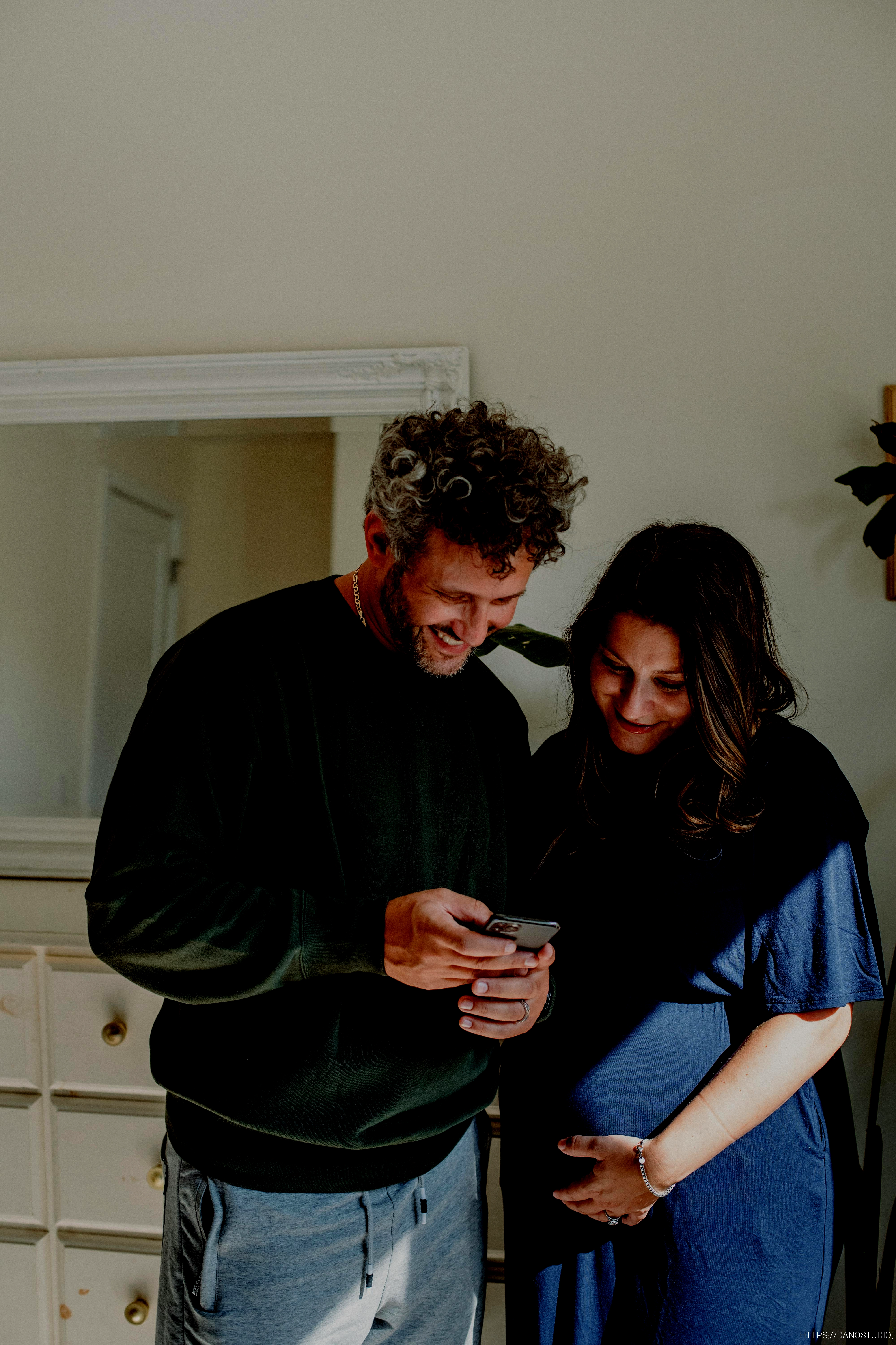 happy pregnant couple sharing smartphone at home